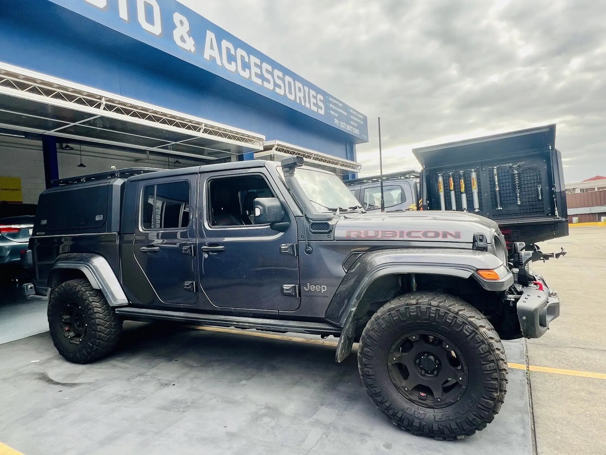Grey Jeep Gladiator Rubicon with snorkel, canopy and mud-terrain tyres outside the Colyton Auto and Accessories workshop